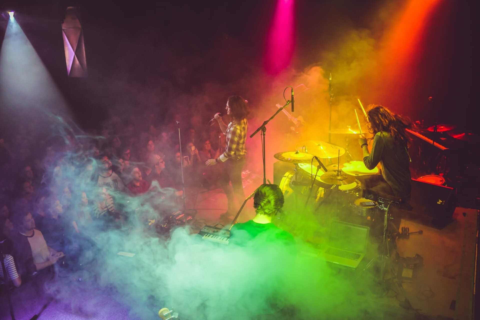 A band performing on stage with rainbow-colored lights flooding them from above
