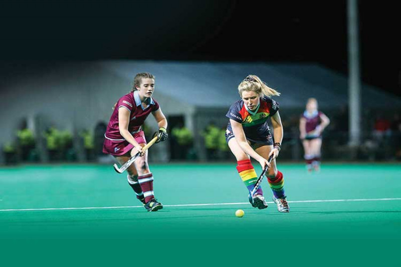 Two hockey players compete for the ball on a floodlit pitch