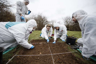 Students in forensic suits examining a field excavation