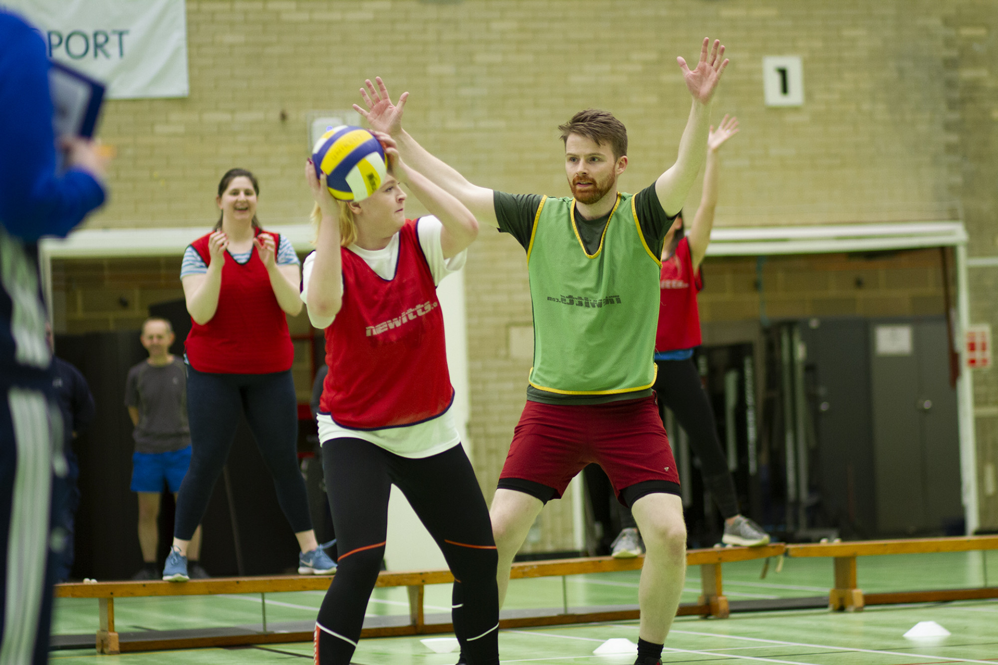 Woman playing netball about to pass the ball while man holds arms up to block the pass