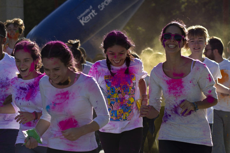 Group of smiling young students jogging from the start line covered in powder paint