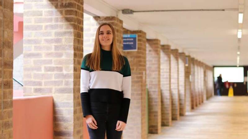 Molly standing in a corridor, light coming through windows to her right