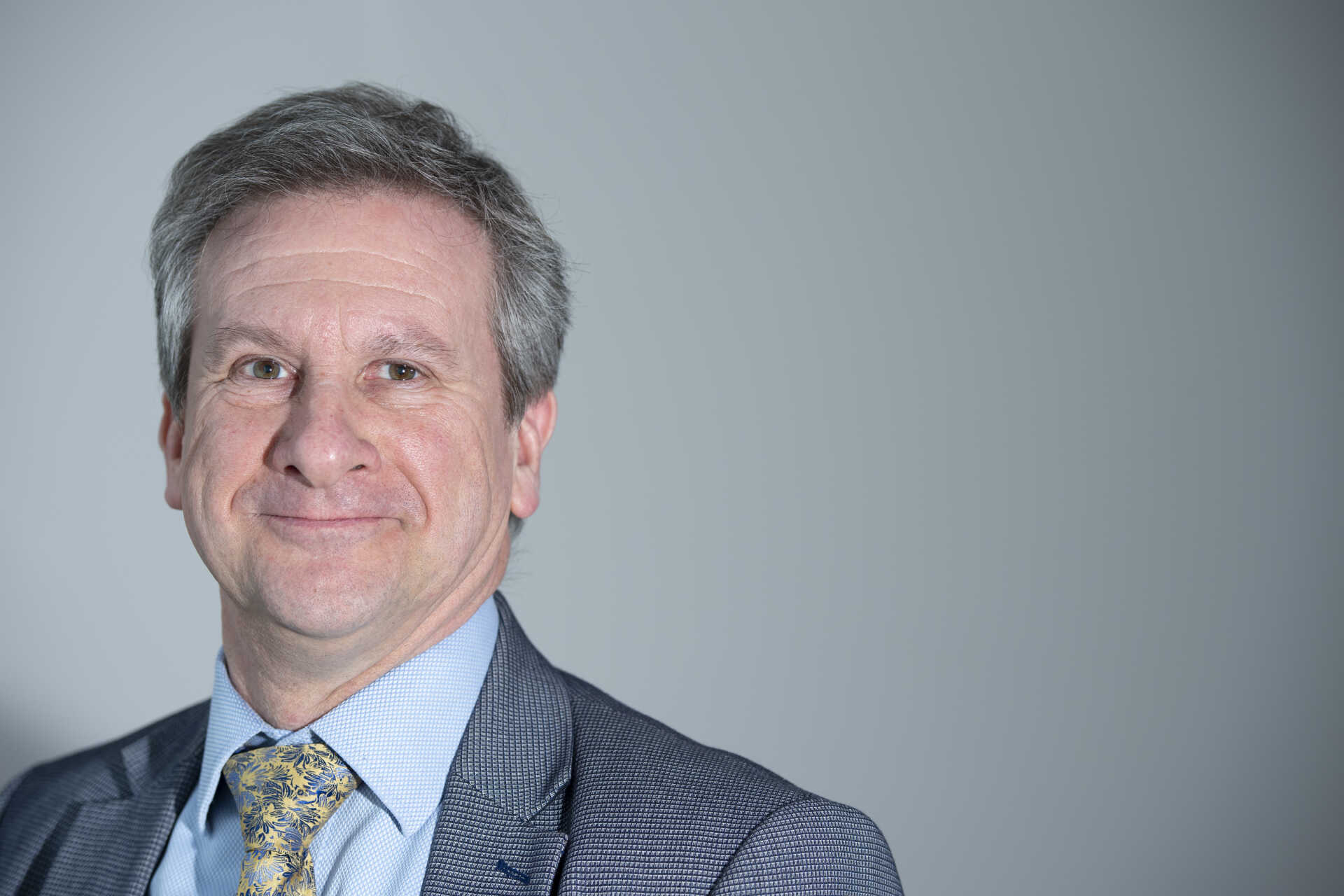 avid stands in front of a grey background, grey hair, suit jacket and blue shirt just visible.