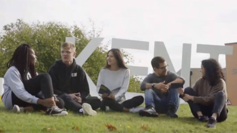 Group of students sitting on grass in front of white KENT letters