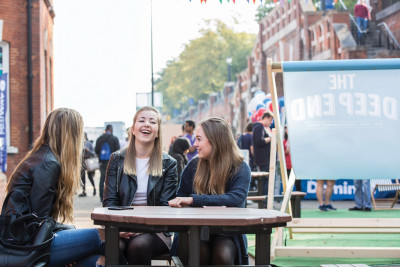 Three female students sitting at an outside table laughing