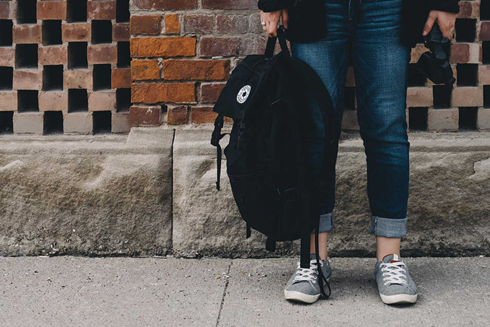 Bottom half of student in jeans, trainers and holding a backpack