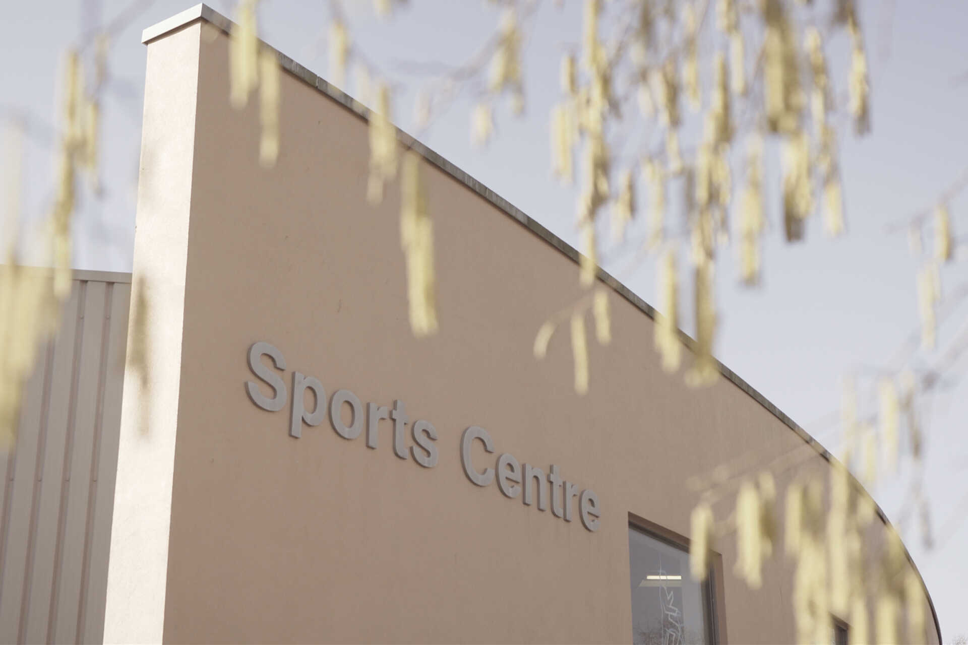 Front view of the corner of the Sports Centre building with overhanging tree branches