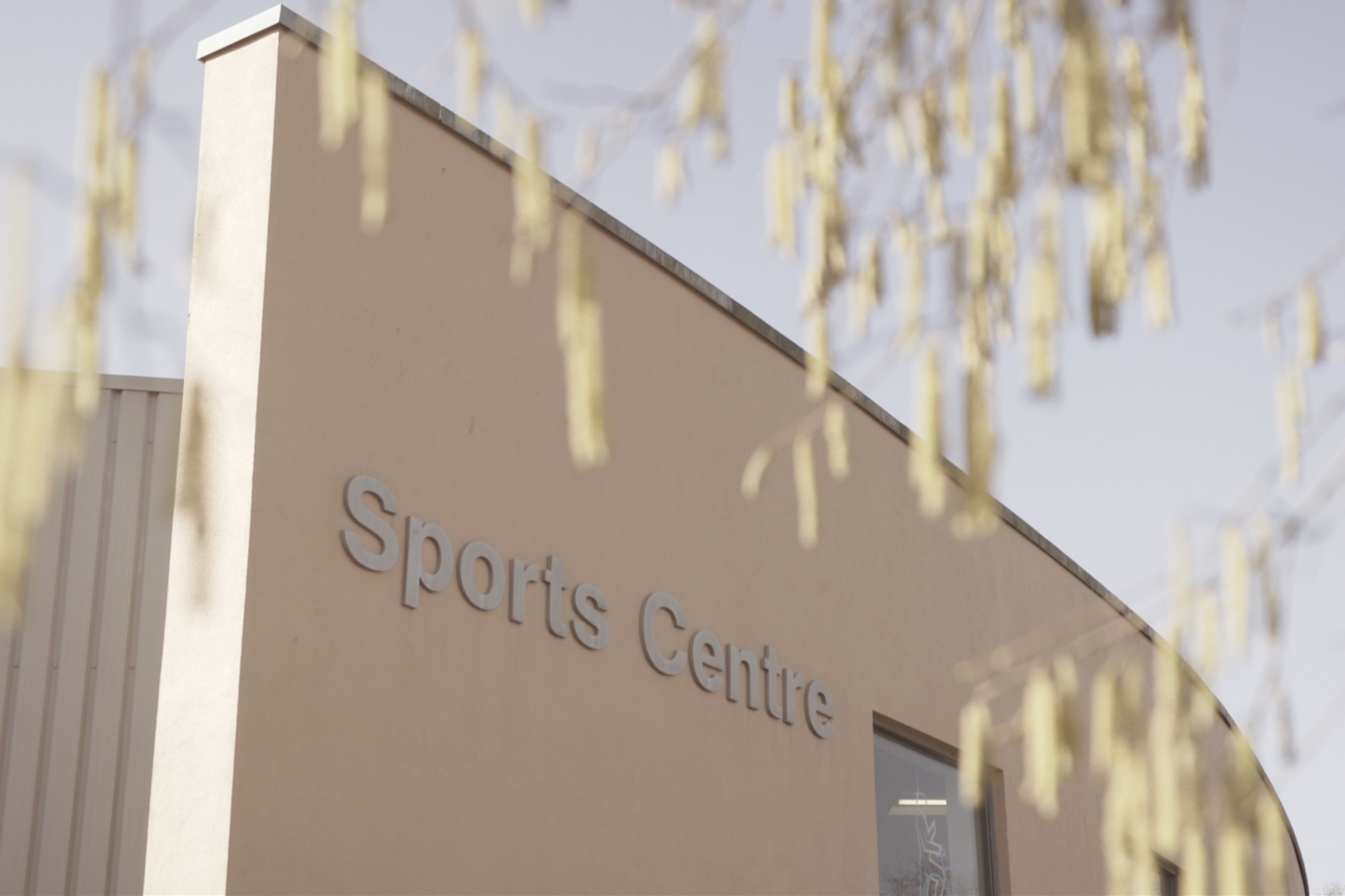 Front view of the corner of the Sports Centre building with overhanging tree branches