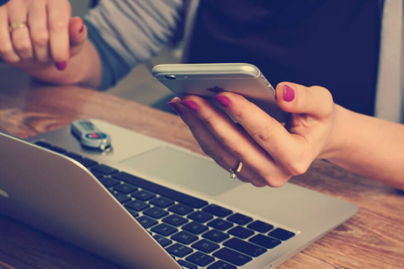 Lady sat at desk in front of laptop holding a phone.