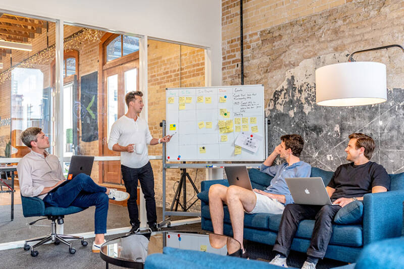 group of people sat on blue sofas with one standing in front of a whiteboard