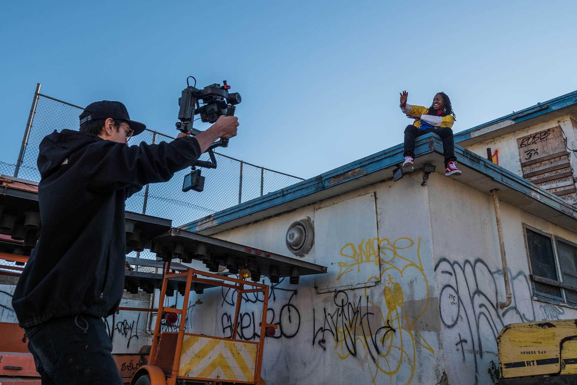 Female sitting on a roof waving at male holding a camera