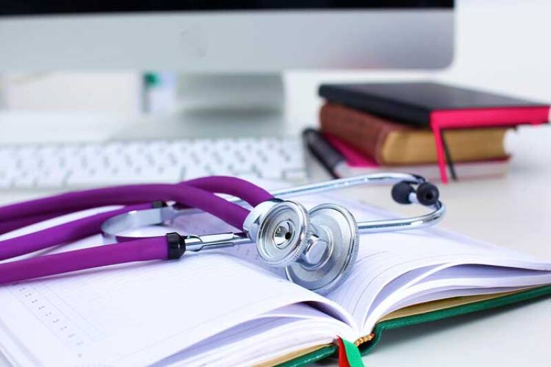 Stethoscope with purple flex on top of open book