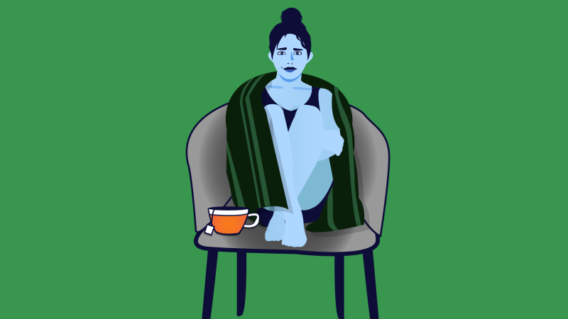 Woman sitting on chair with blanket and cup of tea.