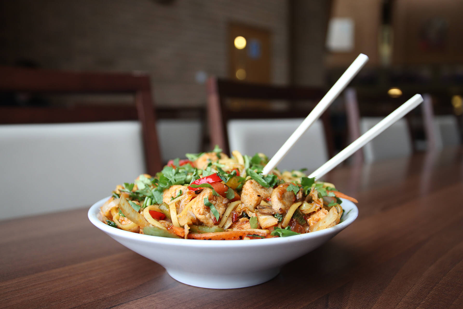A chicken, vegetable and noodle stir fry in a bowl with two chopsticks