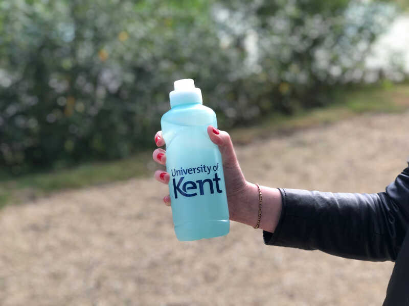 An outstretched hand holding a Kent branded reusable water bottle