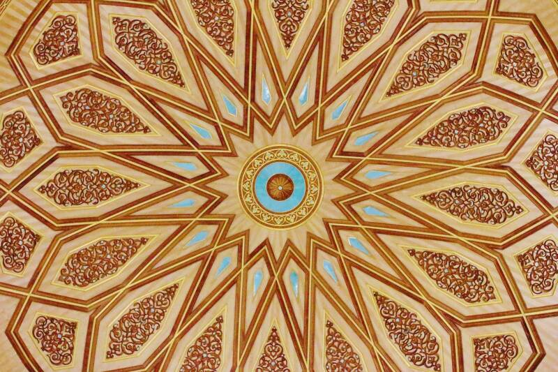 Image of the intricate red and gold design on the interior of a dome inside a mosque.