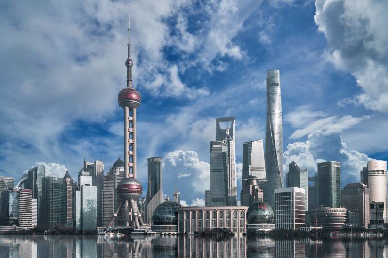 The Shanghai skyline. Blue sky and white clouds can be seen above the modern skyscrapers, reflected in the river.