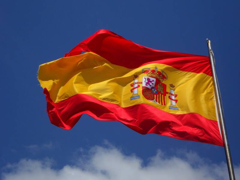 Red and gold Spanish flag, flying in the breeze against a blue sky.