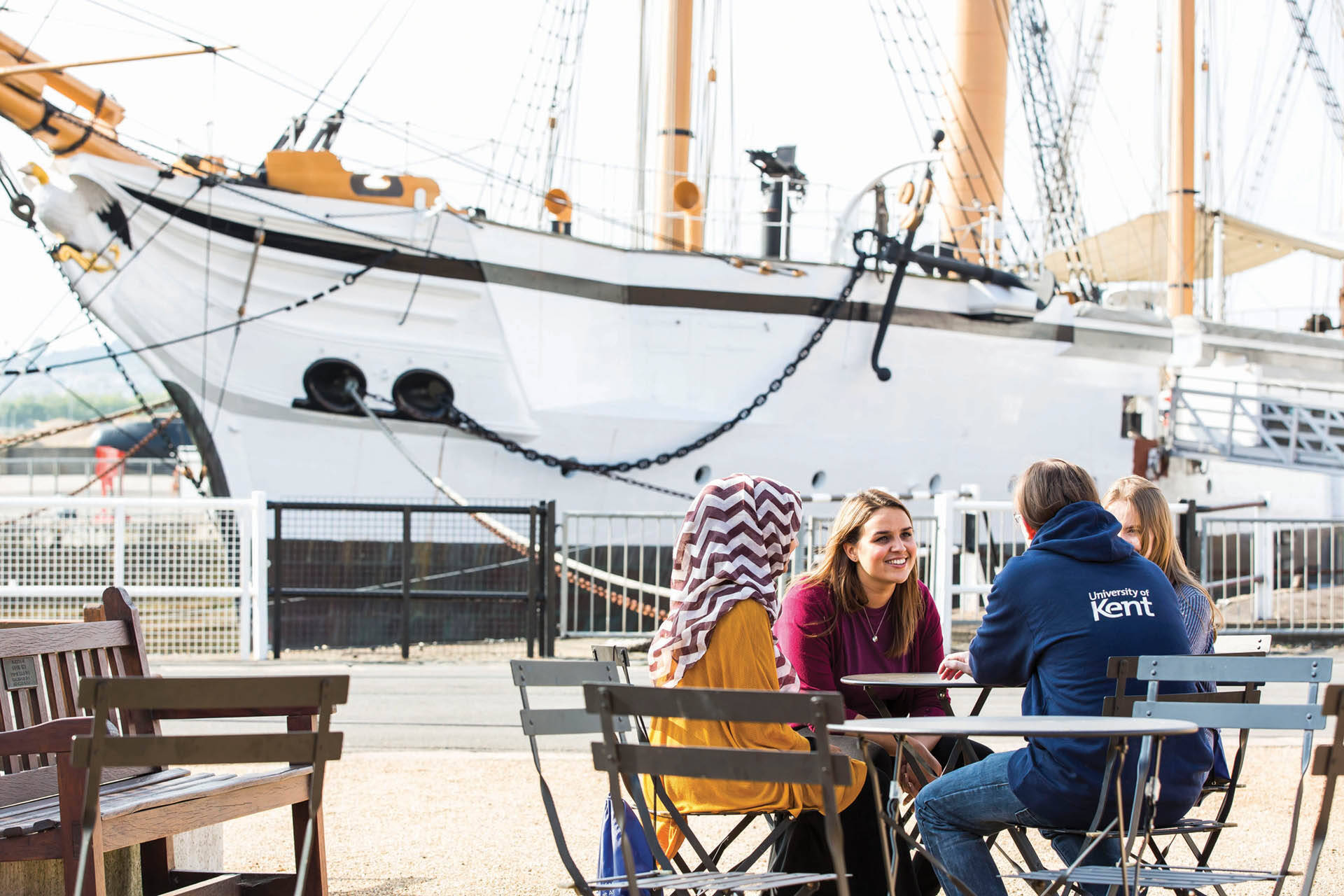 4 students sitting at a table in front of a ship in Medway dockyard