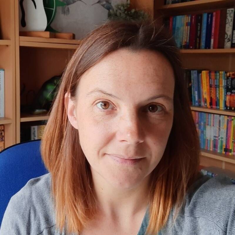 Catherine sits in front on a bookcase