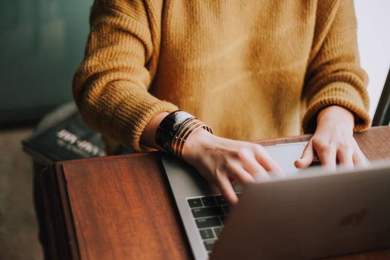 Person in yellow jumper typing on a laptop