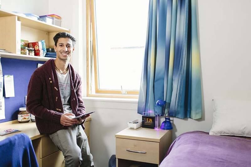 Male student standing in a Pier Quays bedroom smiling at camera