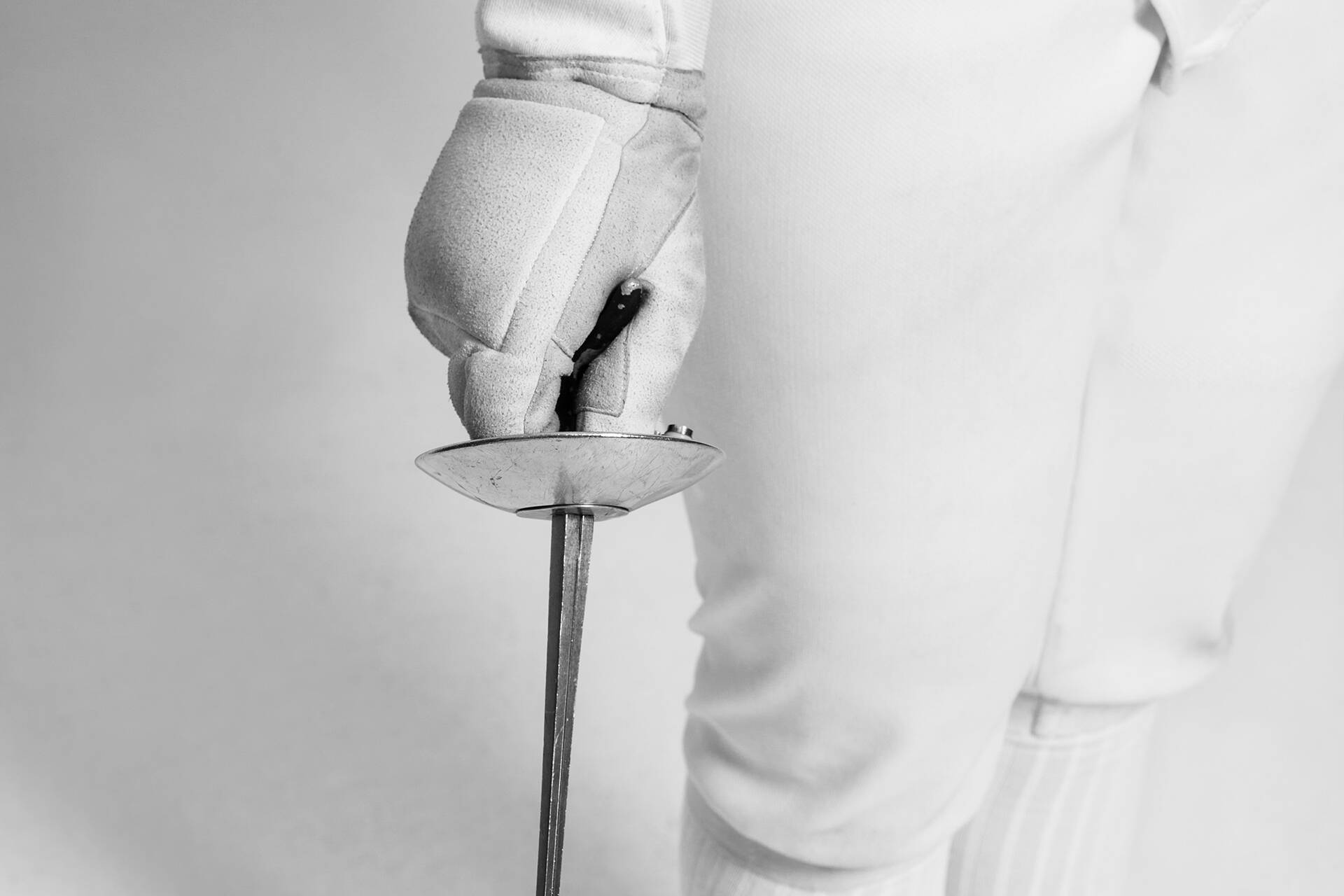 Close-up shot of fencer in full kit holding sword with gloved hand