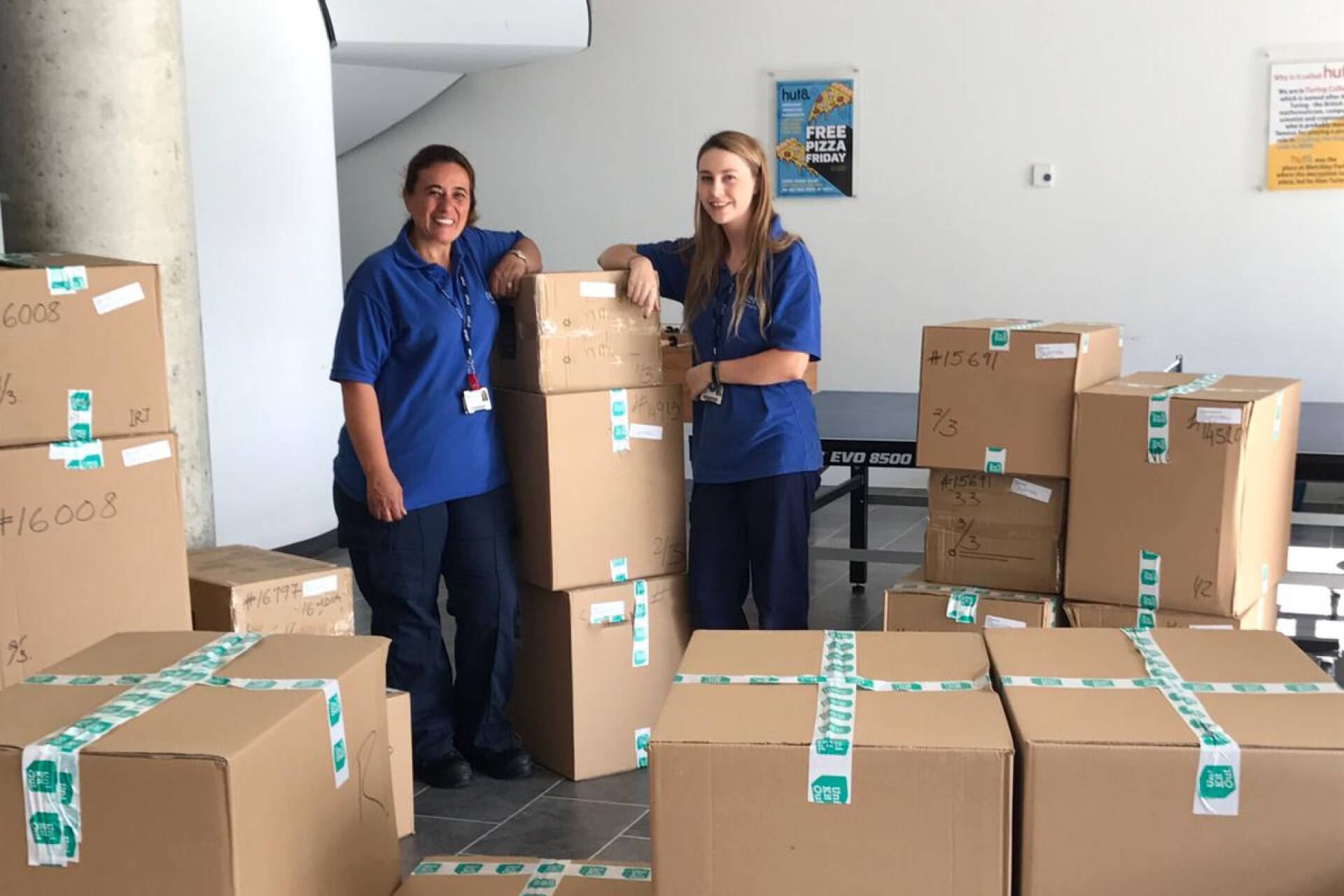 Two Housekeepers pose with UniKitOut delivery boxes in Hut8