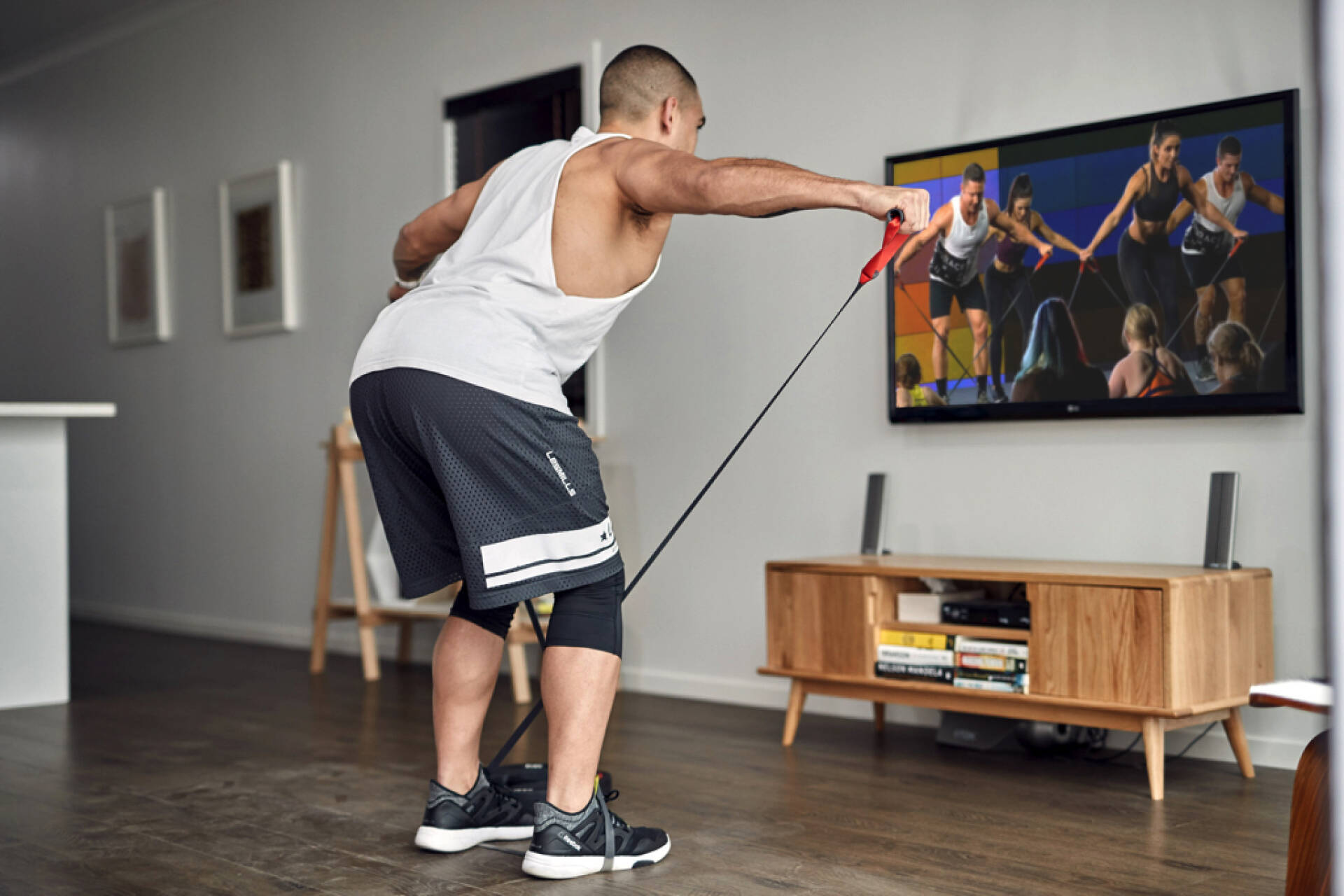 Man watching a workout video at home, following the movements with resistance bands