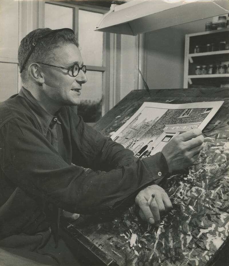A black and white photograph of Giles working at his easel in his early career.