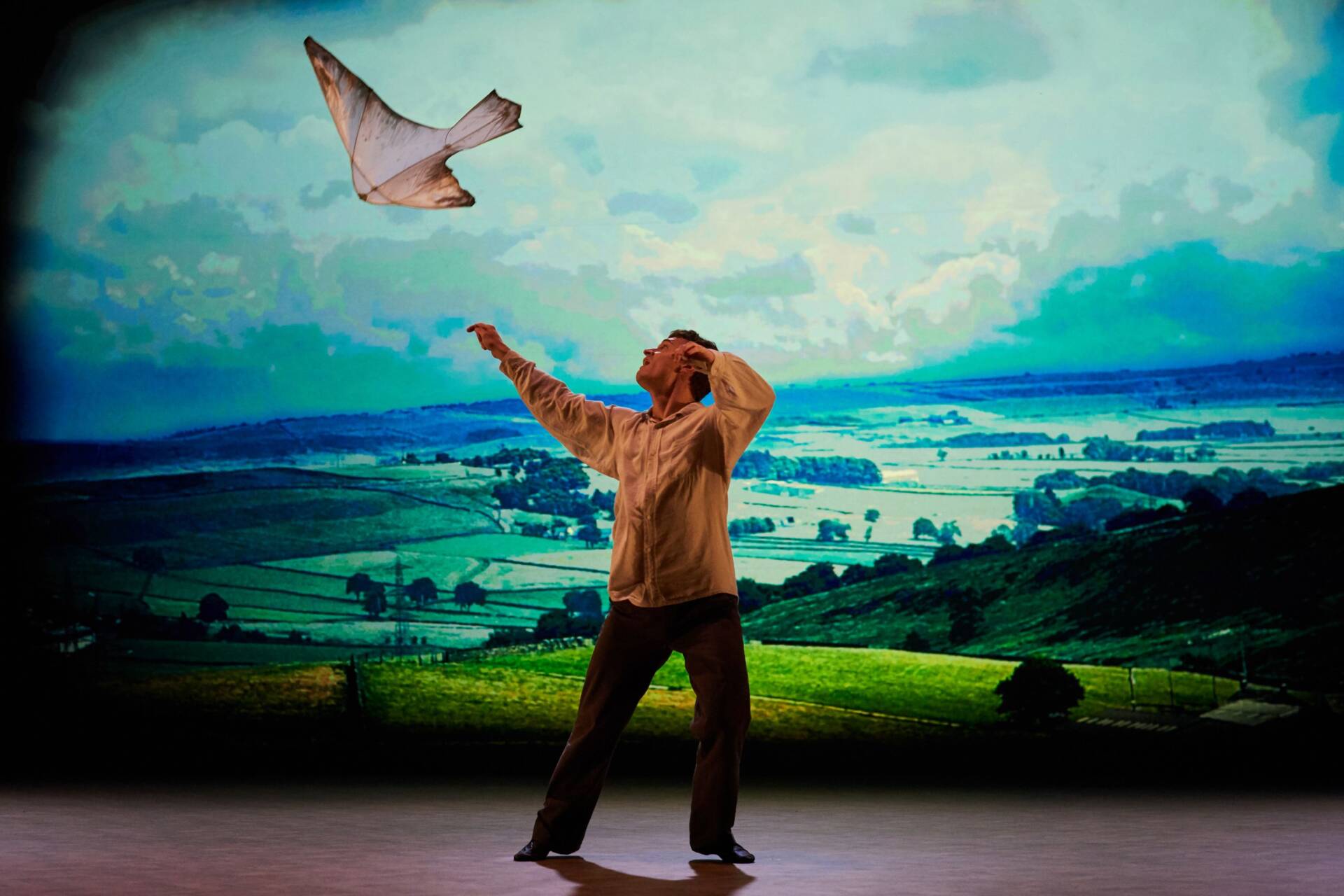 A man on a stage looks up at a kestrel kite