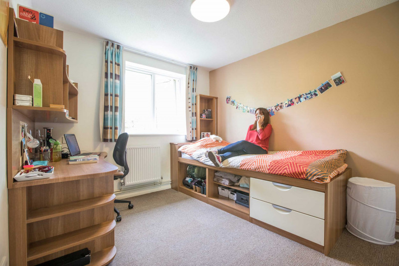 Female student sitting on bed using mobile in Park Wood House bedroom