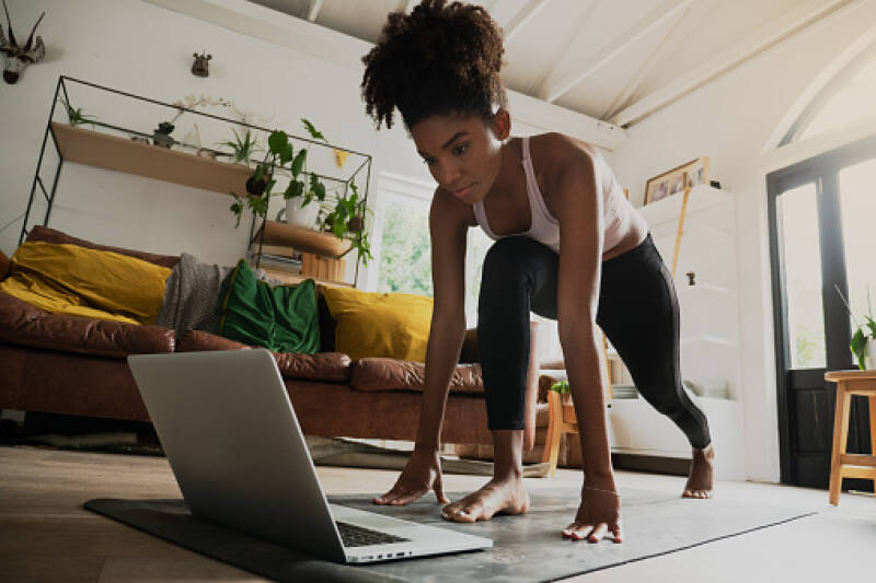 A lady is in her living room working out whilst watching a class.