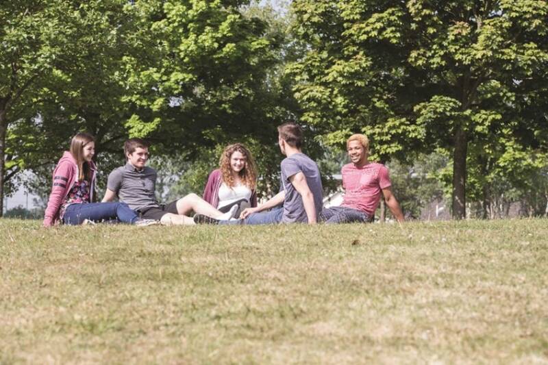 A group of friends sitting on the grass, talking and smiling on a hot sunny day