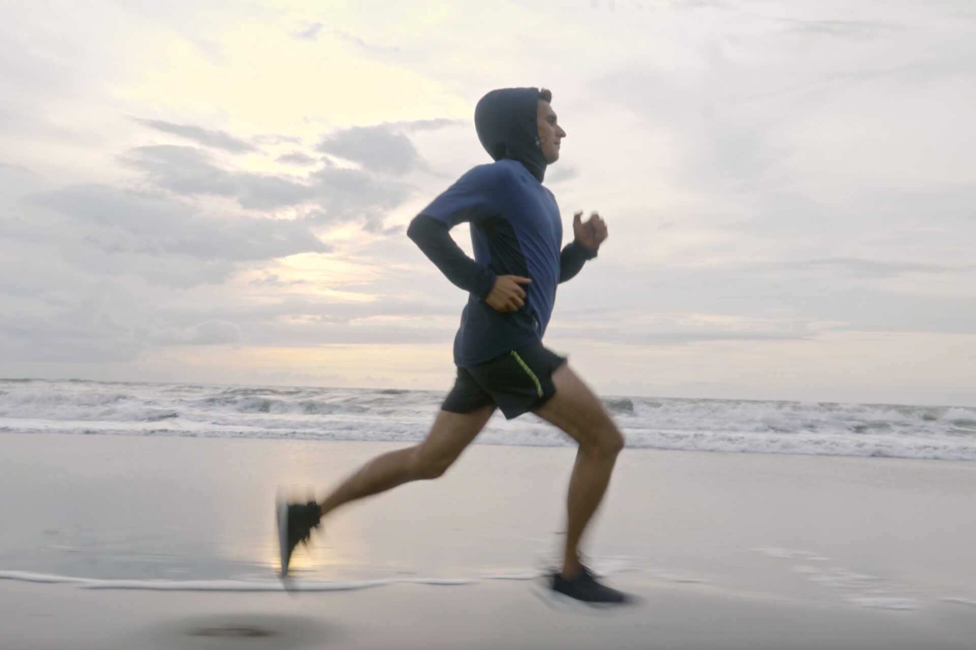 Man in hoodie running across the beach on a cloudy day