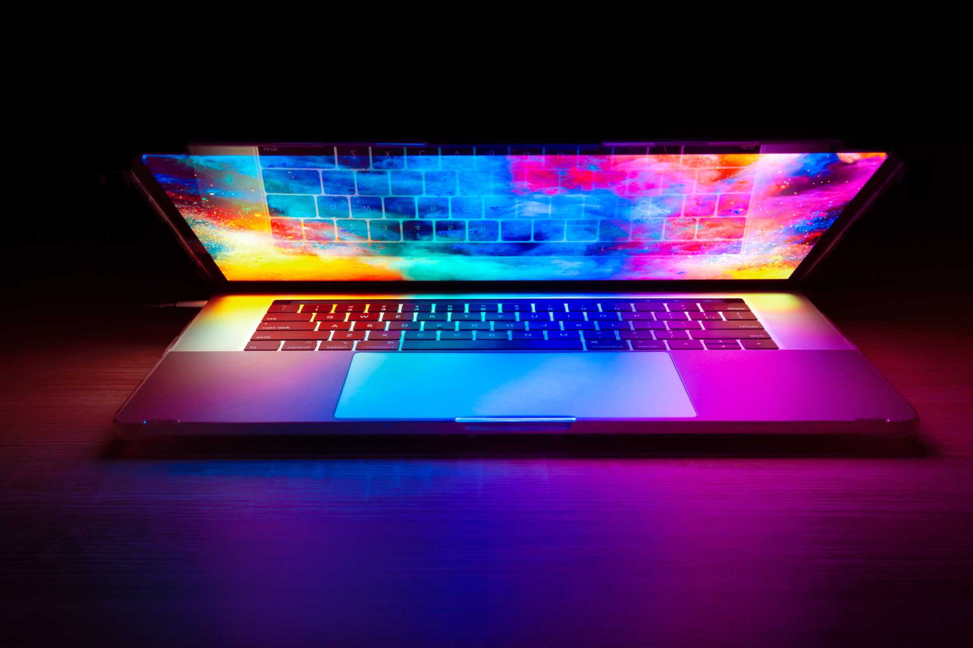 Opening laptop filled with rainbow colours against a dark background