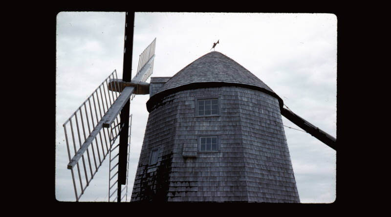 A black and white photograph of a mill, showing the top of the tower and blades
