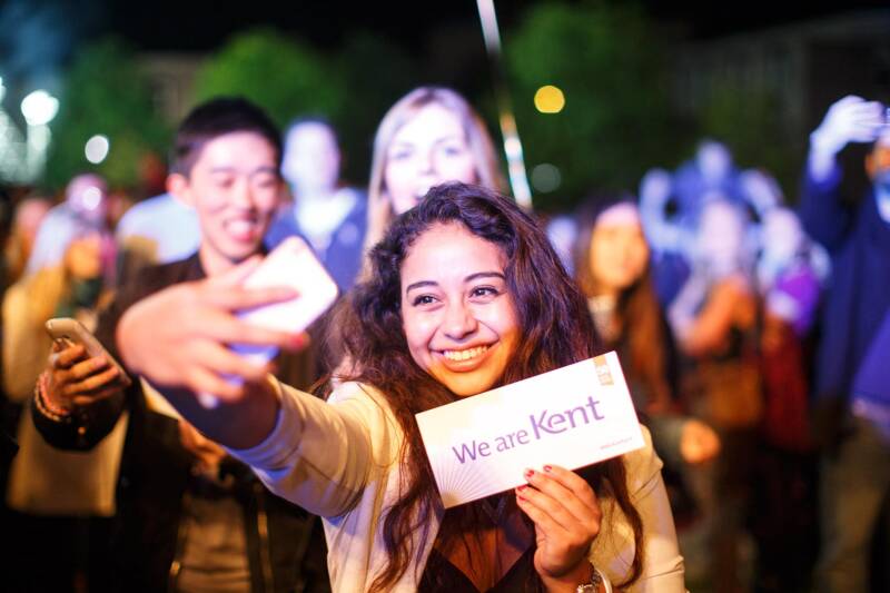 Kent student taking a selfie with a We are Kent board
