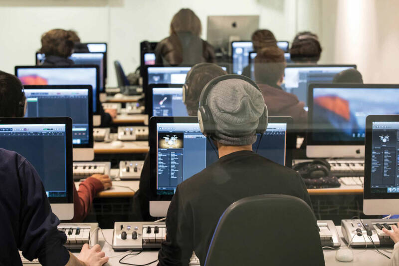 Student wearing a beanie hat and headphones, their back visible, seated at iMac