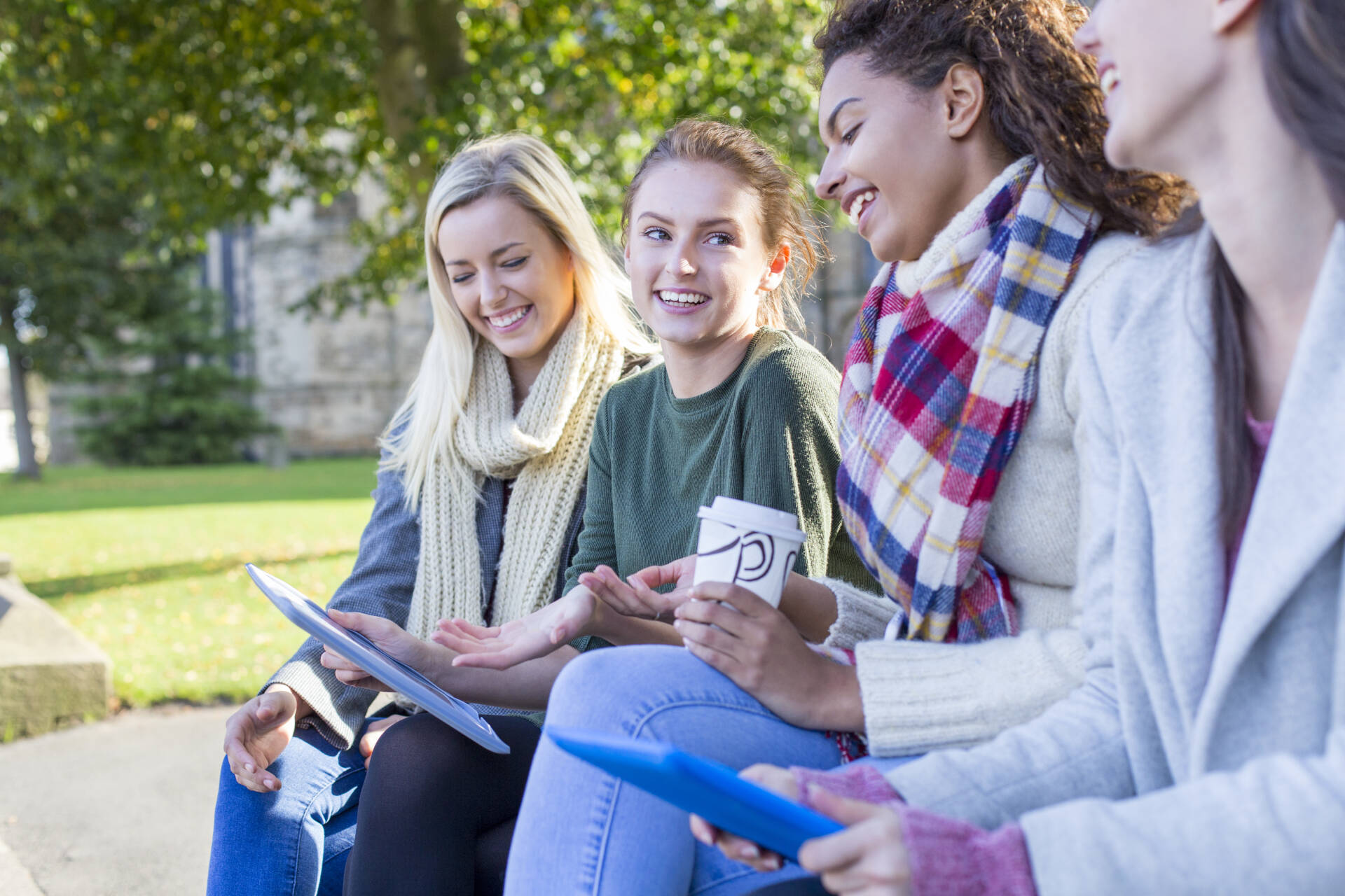 Four female students talking, laughing and drinking coffee outside