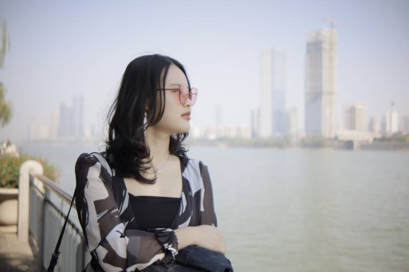 Min-Zhe Qiu pictured sitting beside some water with tall buildings in the background