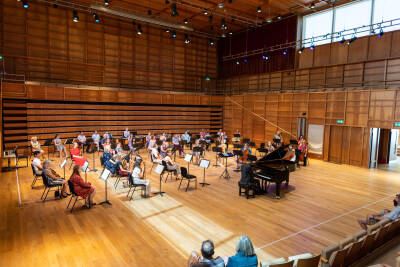 Group of orchestral musicians in a concert-hall; a pianist plays a grand piano in front