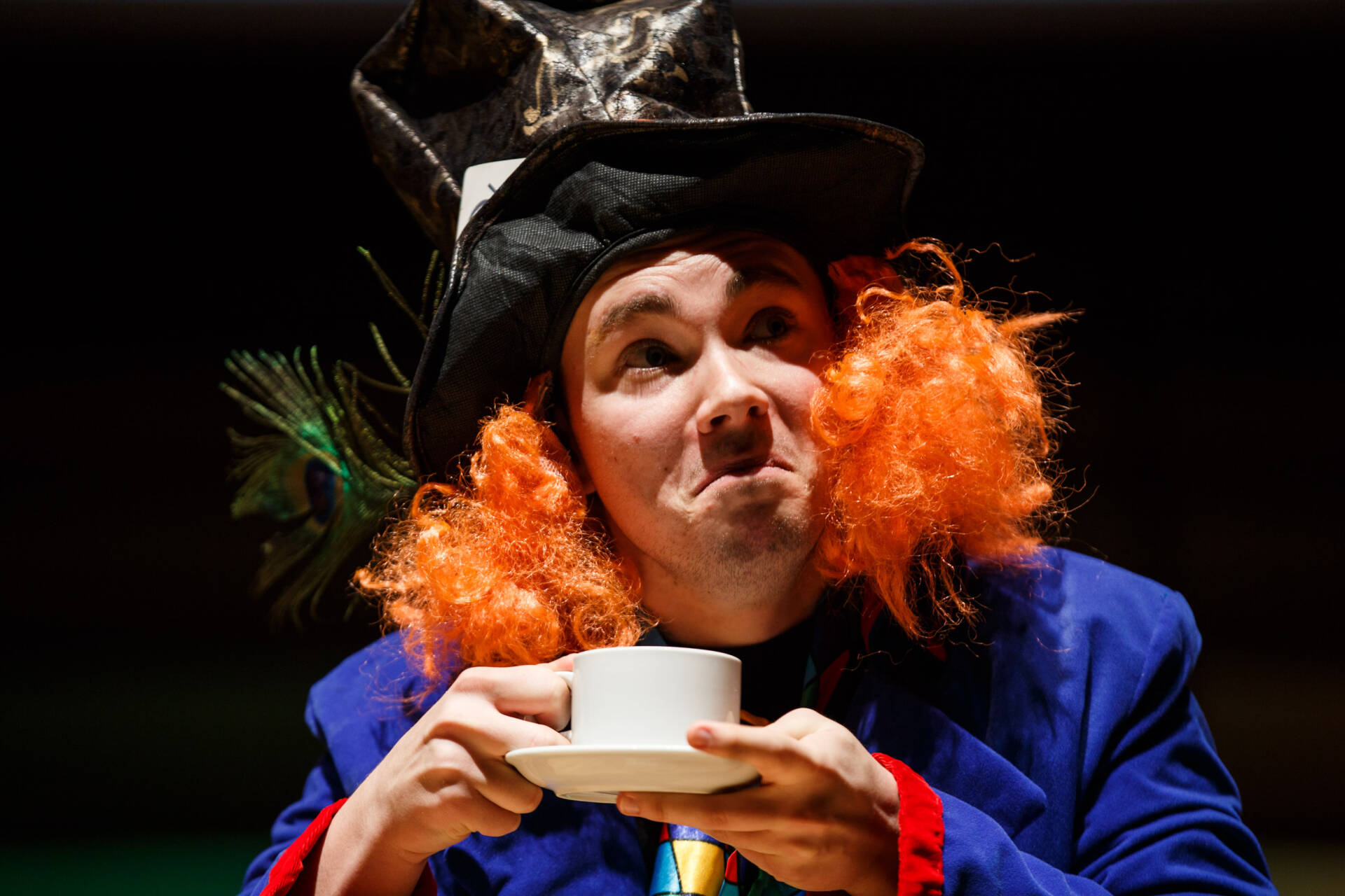 Costumed performer in top hat and orange wig holding a cup and saucer