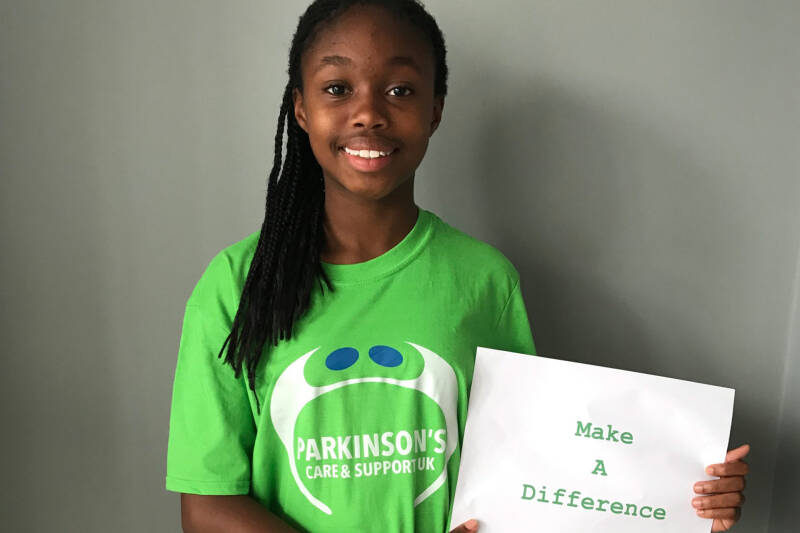 Parkinson's Care and Support UK volunteer Kelize holding a sign which reads Make A Difference