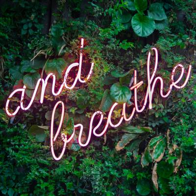 neon lights spelling 'just breathe' in a living wall of plants