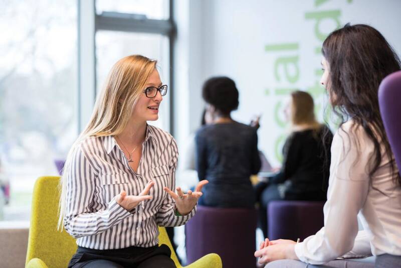 Two professional women talking, one facing the camera and one facing away.