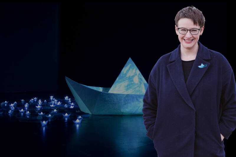 Person stands in front of illuminated boat art installation