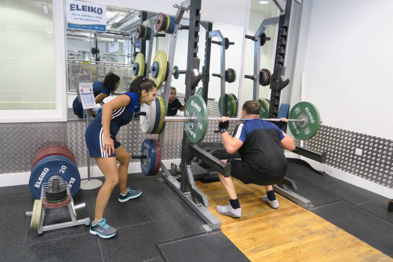 Personal Trainer Laetitia providing advice to a client while using the squat rack in the gym