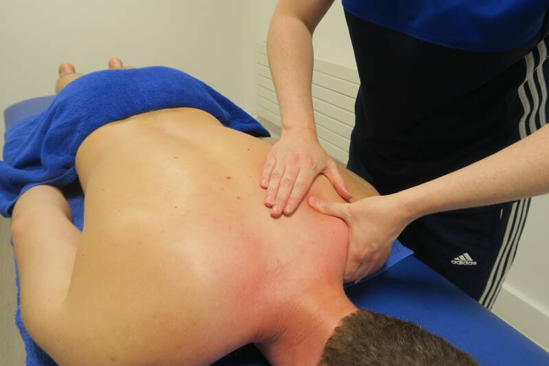 Qualified massage therapist assessing a clients shoulder during a massage appointment.