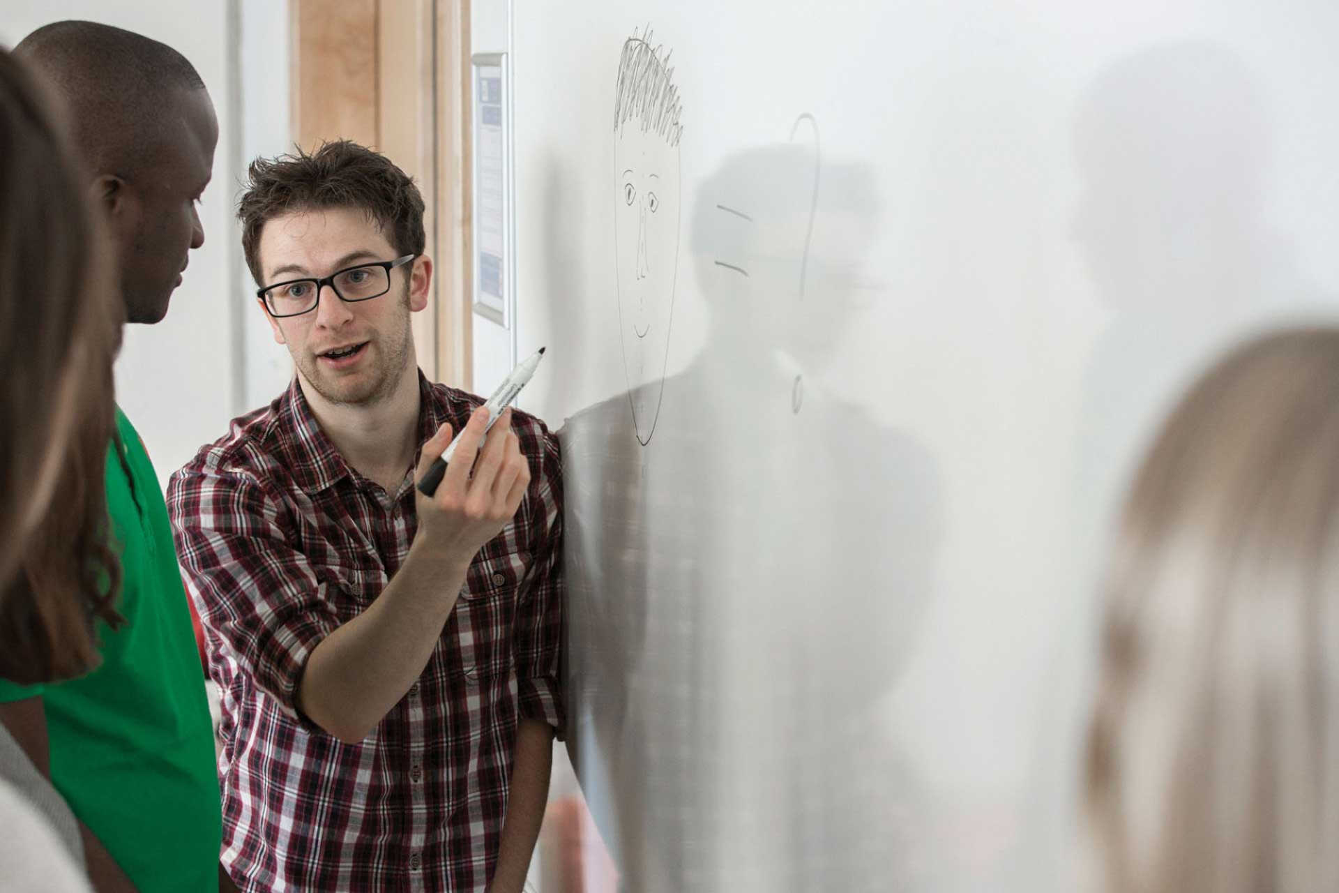 Student works on a white board in front of a group of postgraduate